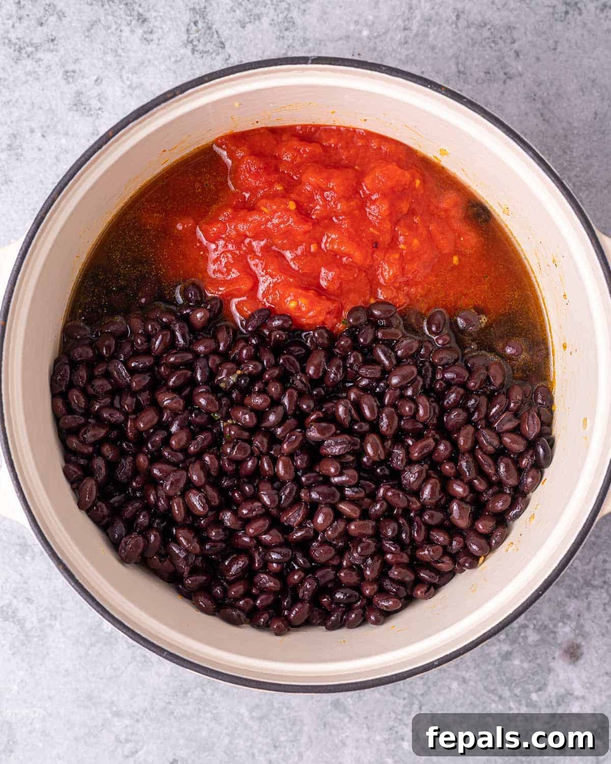 Adding black beans and diced tomatoes into the pot with other stew ingredients.