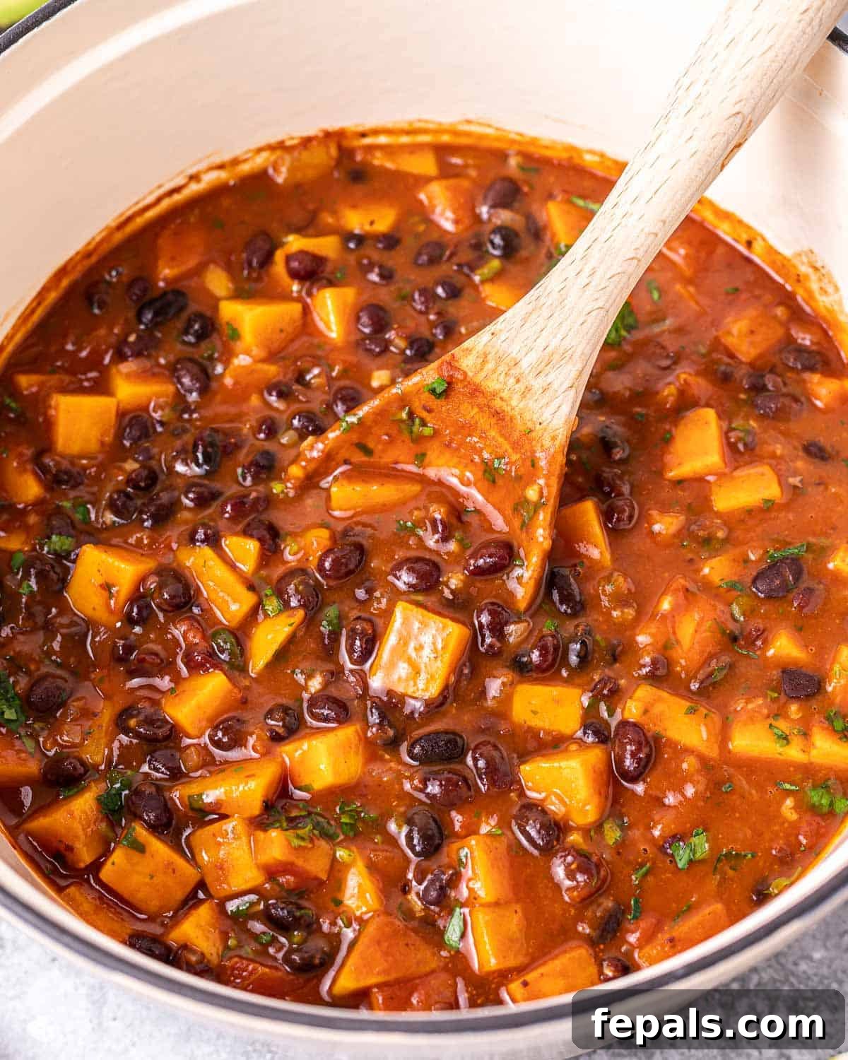 Using a wooden spoon to stir the chili mixture in the pot, adding the lime-flour thickener.