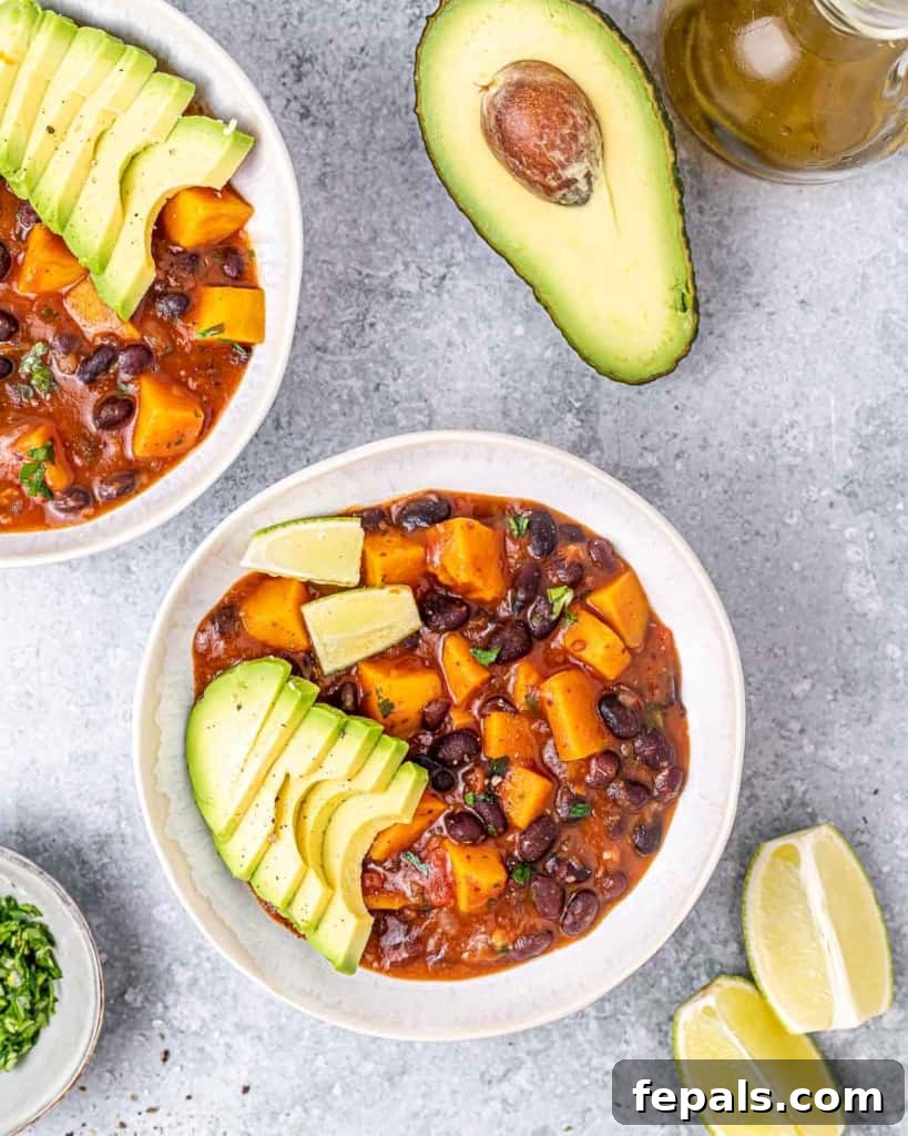 Top view of two bowls of black bean sweet potato stew in white round bowls, garnished with fresh herbs.