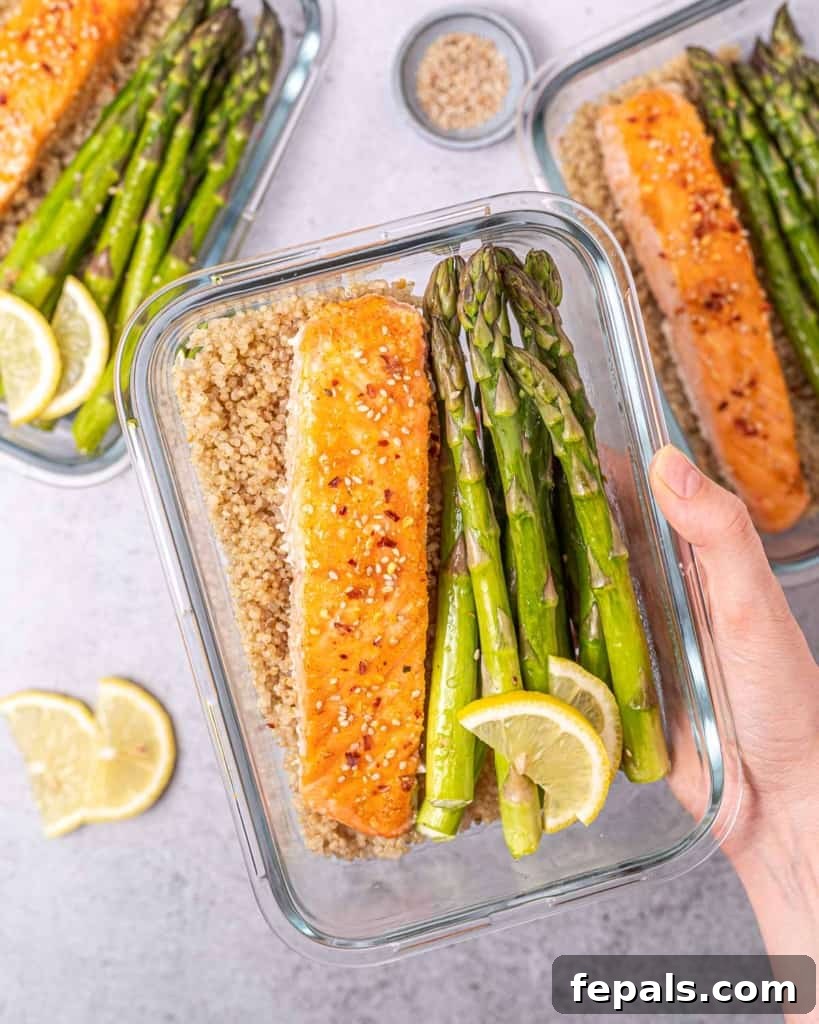 Woman's hand holding a glass container filled with salmon, asparagus, and quinoa.