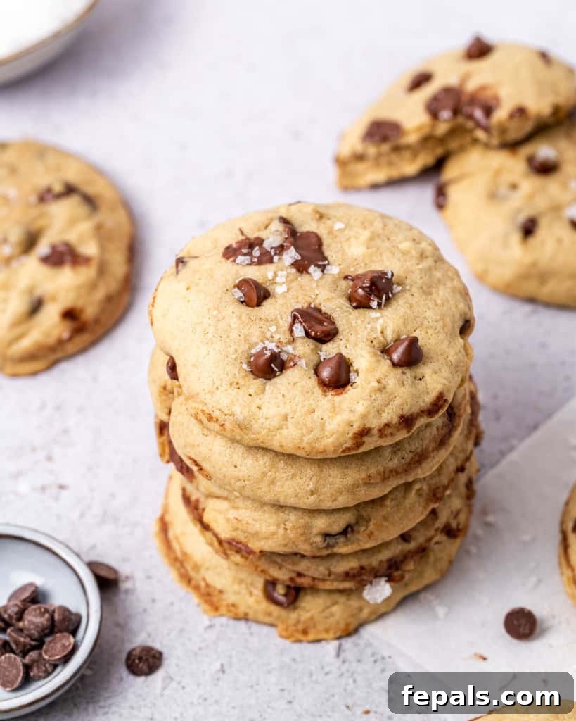 A beautifully composed photograph showcasing several vegan chocolate chip cookies neatly stacked on top of each other, emphasizing their appealing texture and plentiful chocolate inclusions.