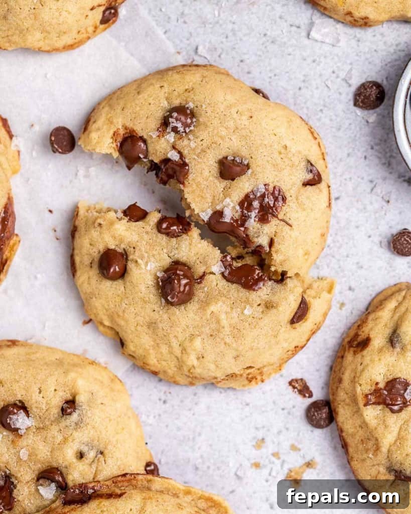 A top-down view of a freshly baked vegan chocolate chip cookie, carefully broken in half on a flat surface to reveal its soft, gooey interior and melted chocolate pieces.