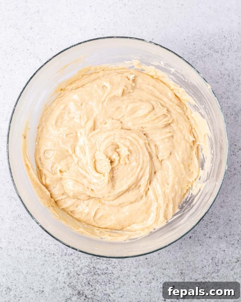 A close-up shot of thick, creamy cookie dough thoroughly mixed in a clear round glass bowl, just before the addition of chocolate chips.