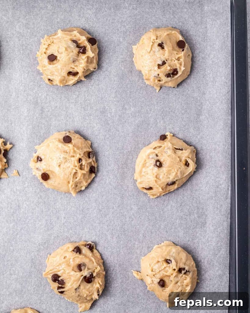 Evenly spaced scoops of raw vegan cookie dough arranged on a parchment-lined baking pan, prepared and ready to be placed in the oven.