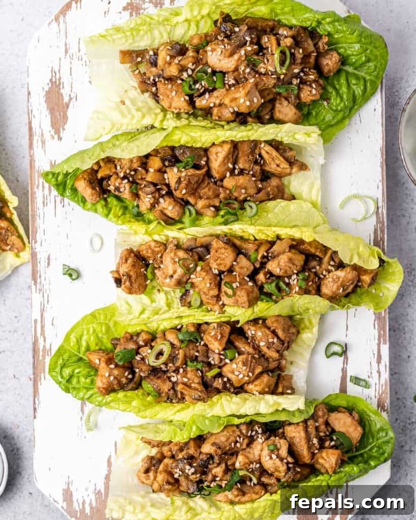 Chicken lettuce wraps on a board, garnished with sesame seeds and green onions.