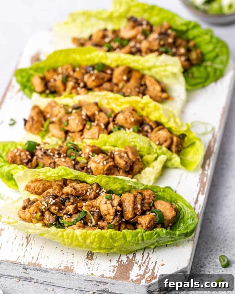 Romaine lettuce leaves filled with a saucy chicken filling, garnished with sesame seeds.