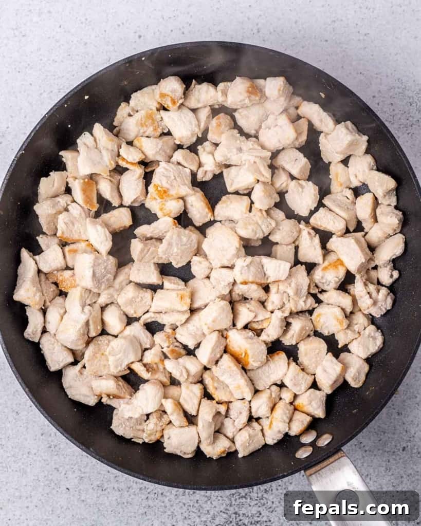 Chicken pieces cooking in a large pan on the stove.