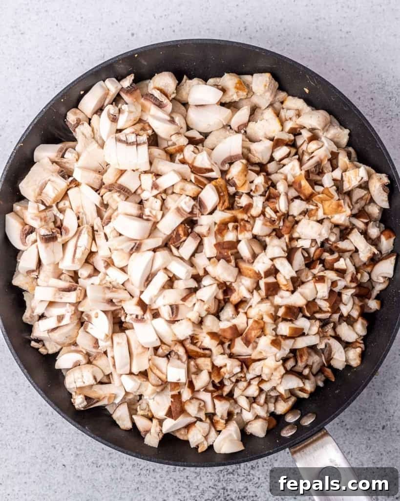 Cooking mushrooms with chicken in a skillet, stirring with a wooden spoon.