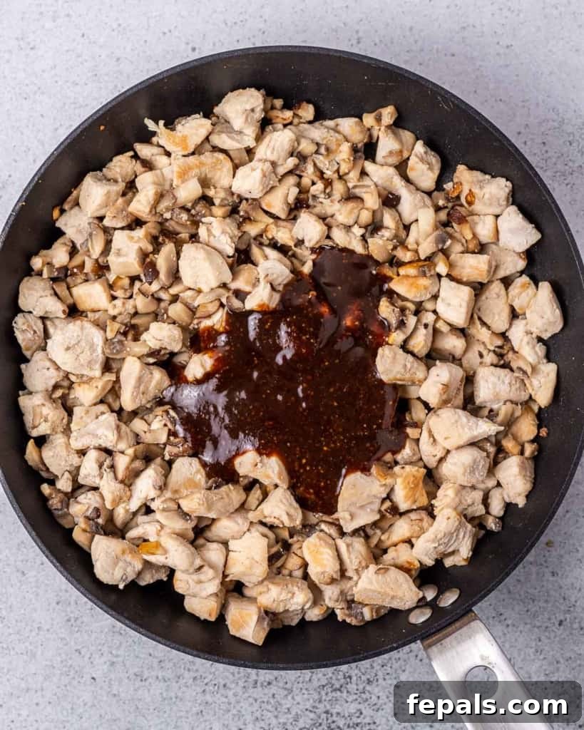 Adding sauce to chicken and mushrooms in a pan, stirring them together.