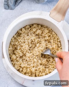 Cooked quinoa in a white pot being fluffed with a fork.