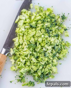 Finely chopped fresh broccoli on a cutting board with a knife nearby.