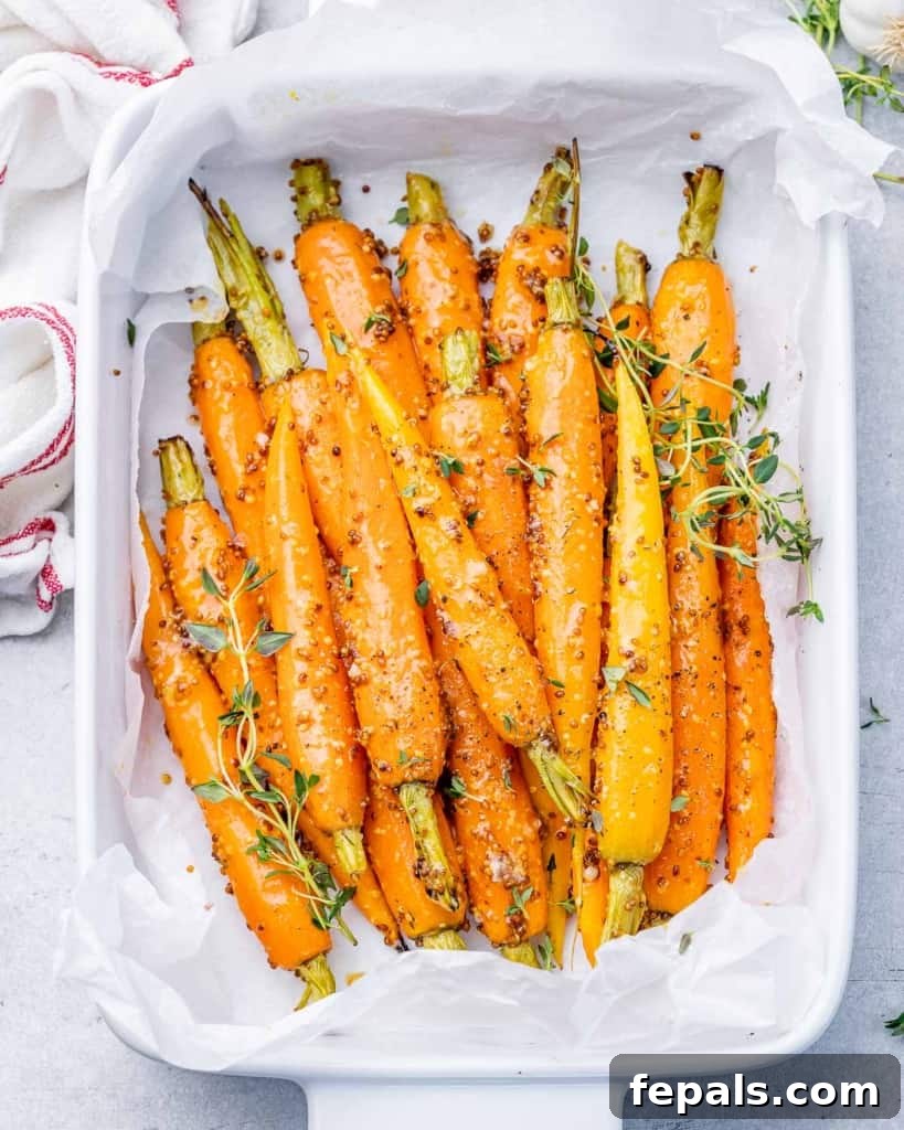 Golden Honey Mustard Carrots 2 Top view of roasted carrots in a honey mustard sauce in a white dish, garnished with fresh herbs.