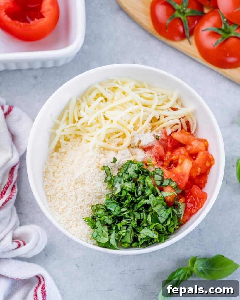 Shredded cheese, basil, and scooped tomato flesh in a white bowl, ready for mixing.
