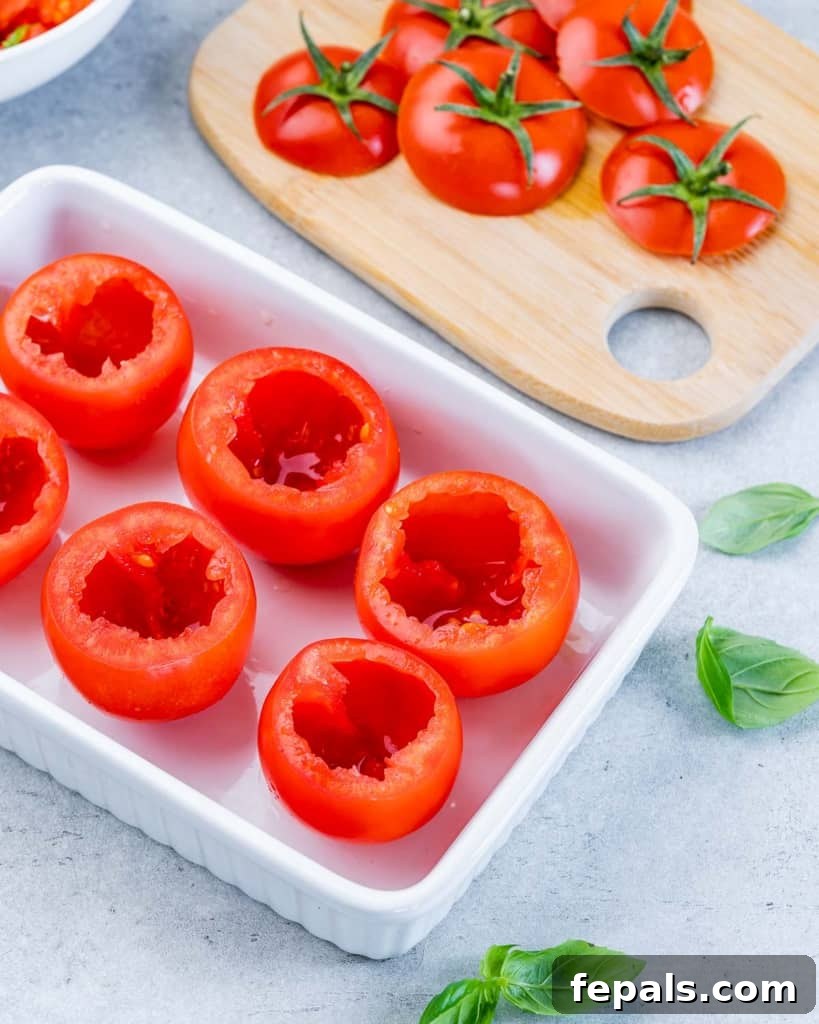 Hollowed-out Roma tomato shells arranged in a white baking dish.