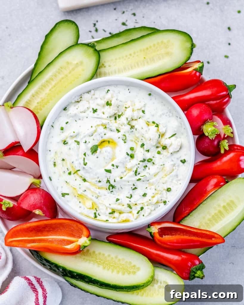 Top view of herbed whipped feta dip in a bowl, surrounded by colorful fresh vegetables like cucumber, bell peppers, and carrots.