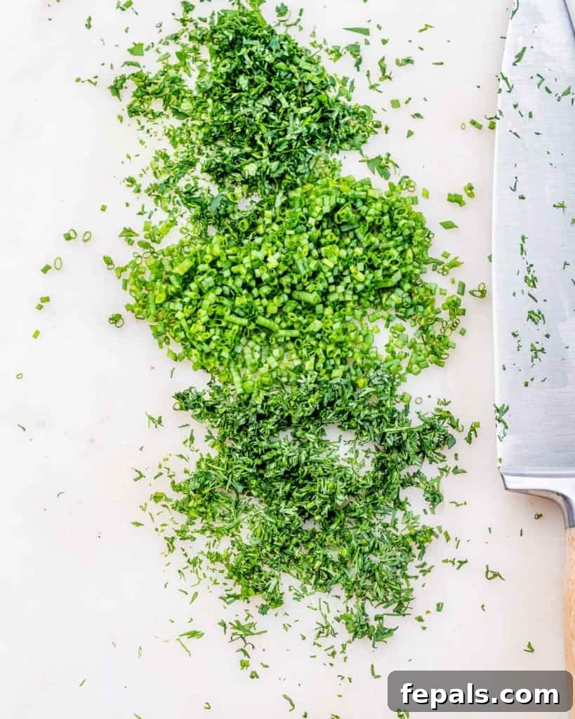 A person's hands finely chopping fresh herbs on a wooden cutting board with a knife.