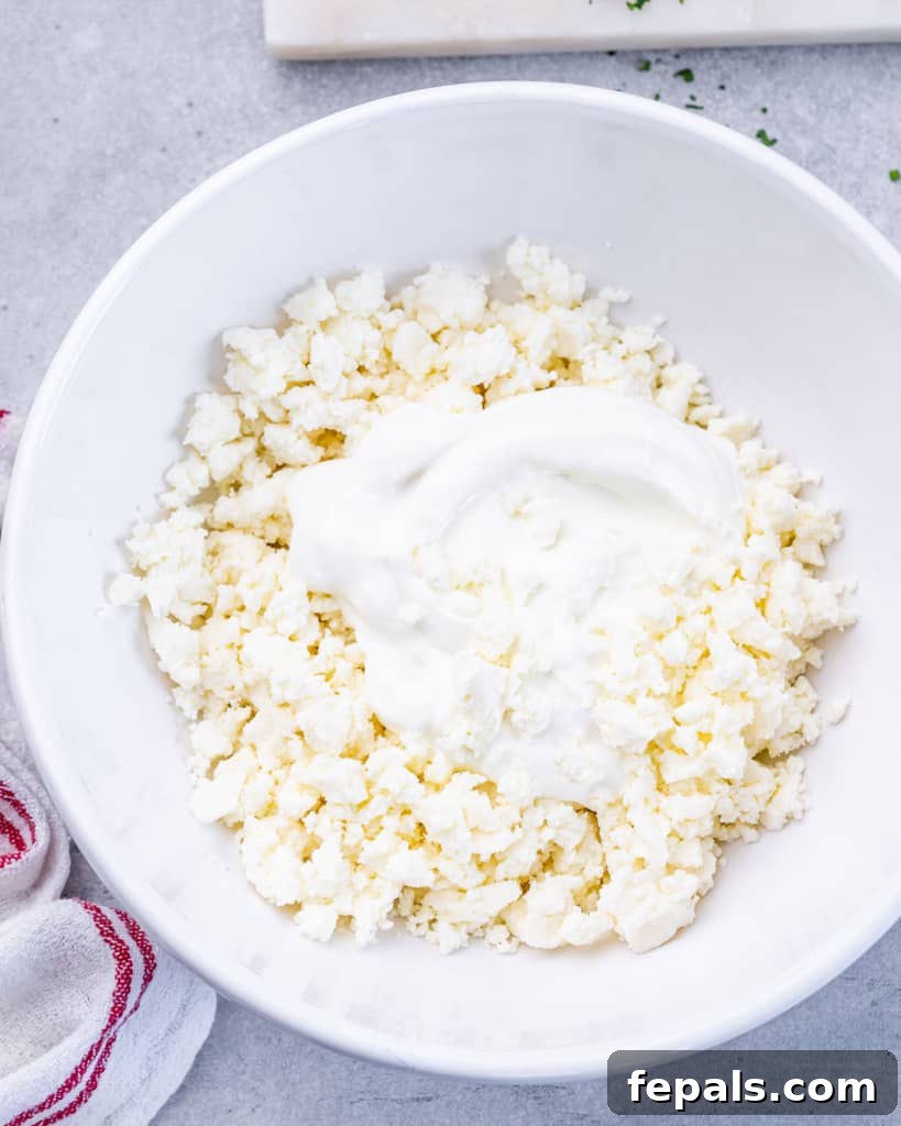 Crumbled feta cheese and Greek yogurt being mixed together in a white bowl with a whisk.
