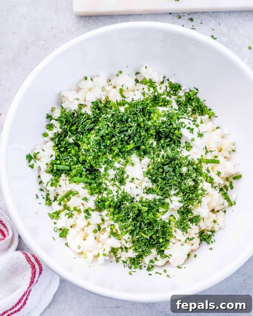 A bowl containing fresh chopped herbs, crumbled feta, and Greek yogurt, ready for mixing.
