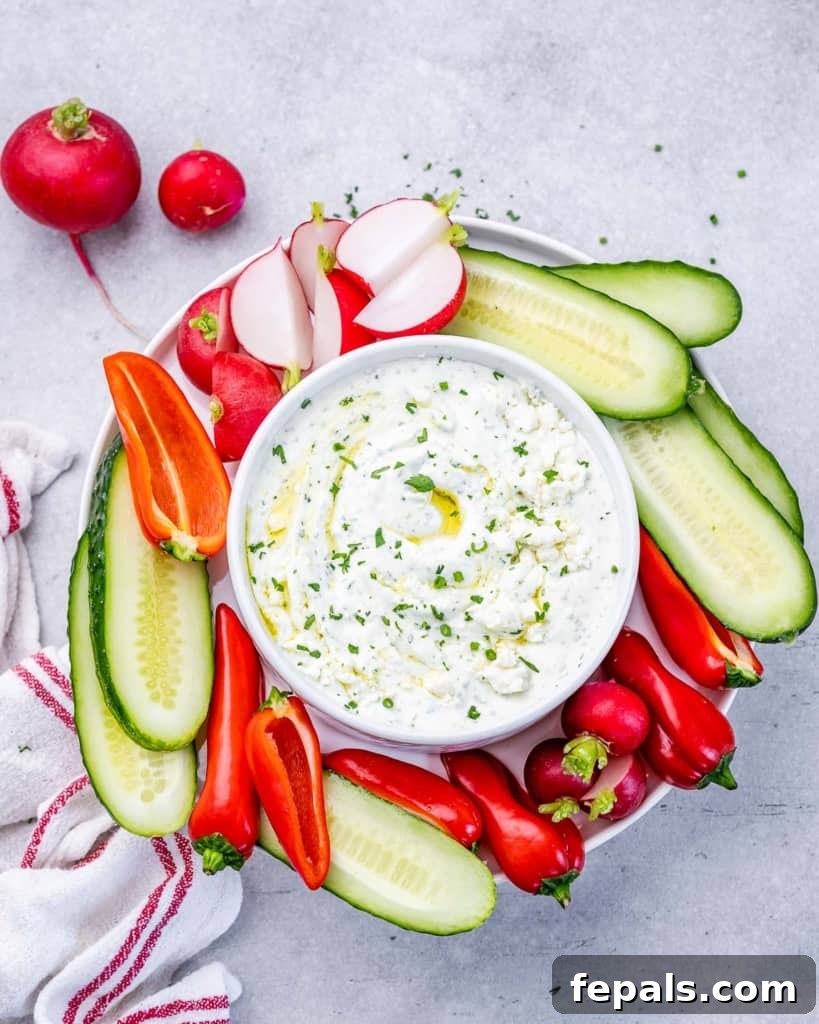Herbed whipped feta dip served in a rustic bowl with an array of fresh, colorful vegetables artfully arranged around it.