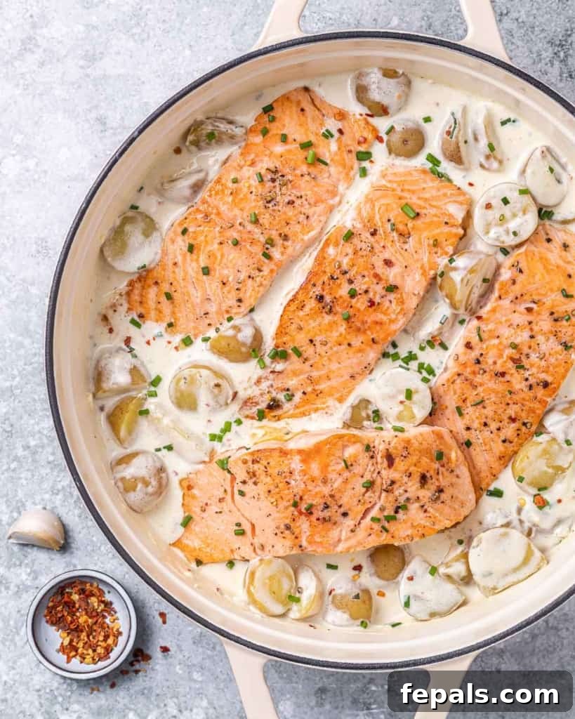 Top view of flaky salmon in a creamy garlic sauce with tender baby potatoes, garnished with fresh herbs in a skillet.
