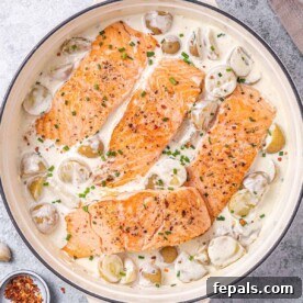 Four seared salmon fillets in a creamy white potato sauce in a skillet, ready to be served.