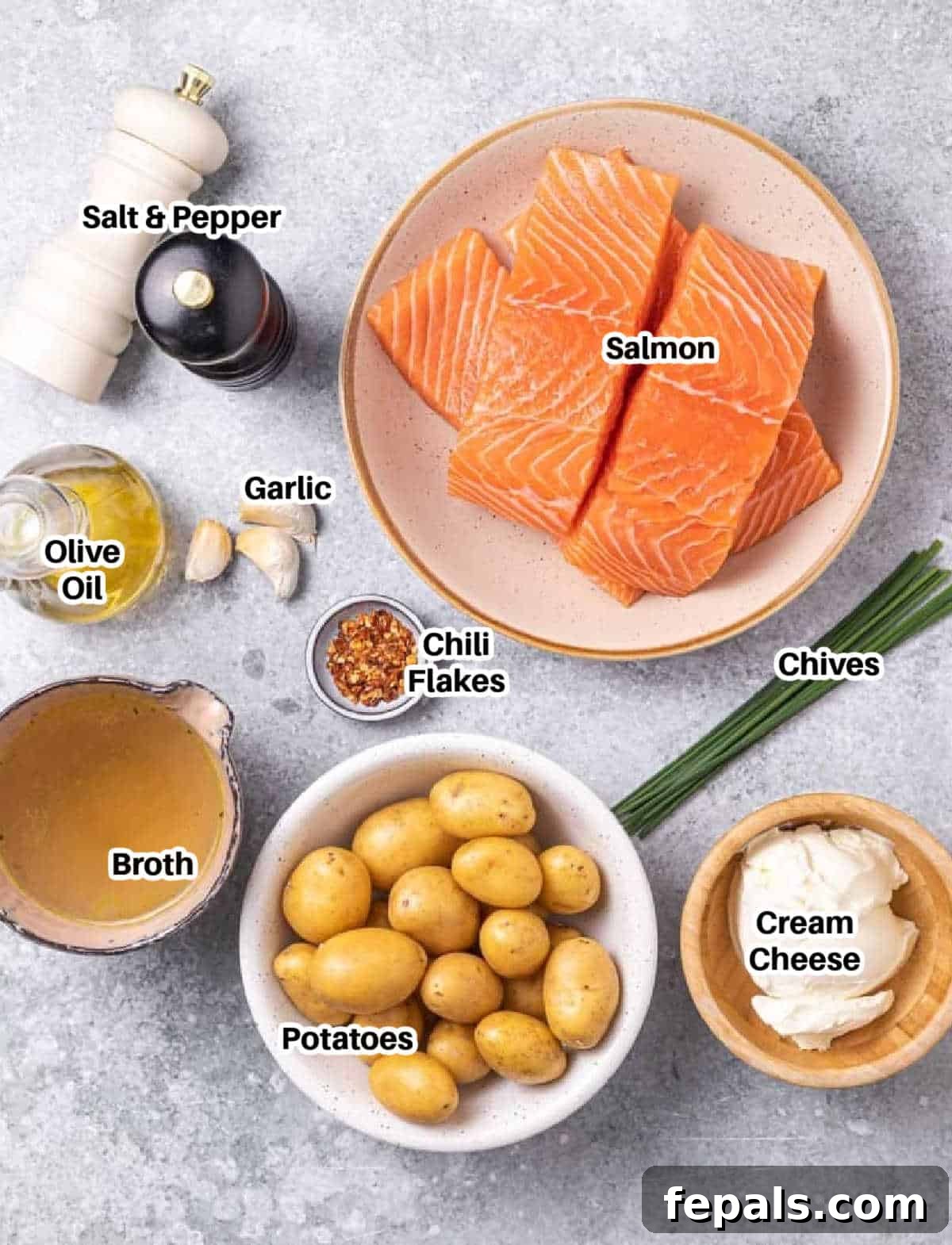 A flat lay of fresh ingredients, including salmon fillets, baby potatoes, cream cheese, garlic, chives, and olive oil, arranged on a surface, ready to make the creamy salmon and potato skillet.