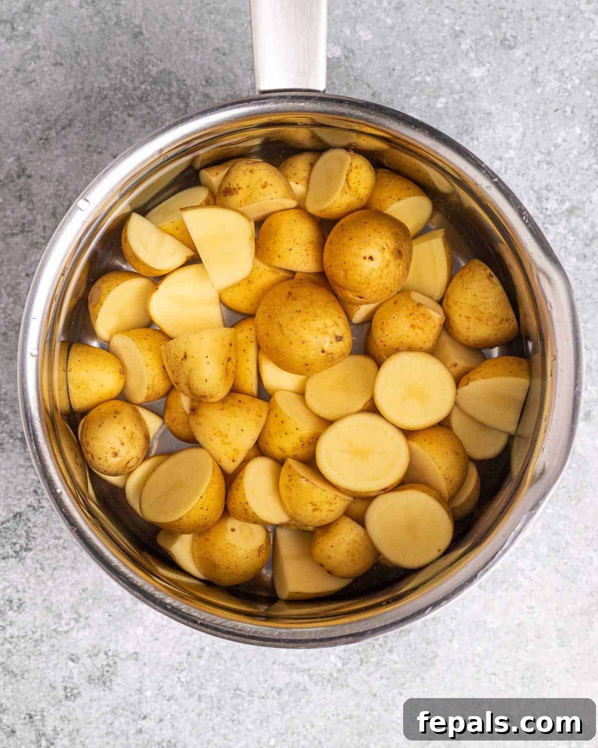 Halved baby potatoes cooked until tender in a pot, ready for the next step of the recipe.