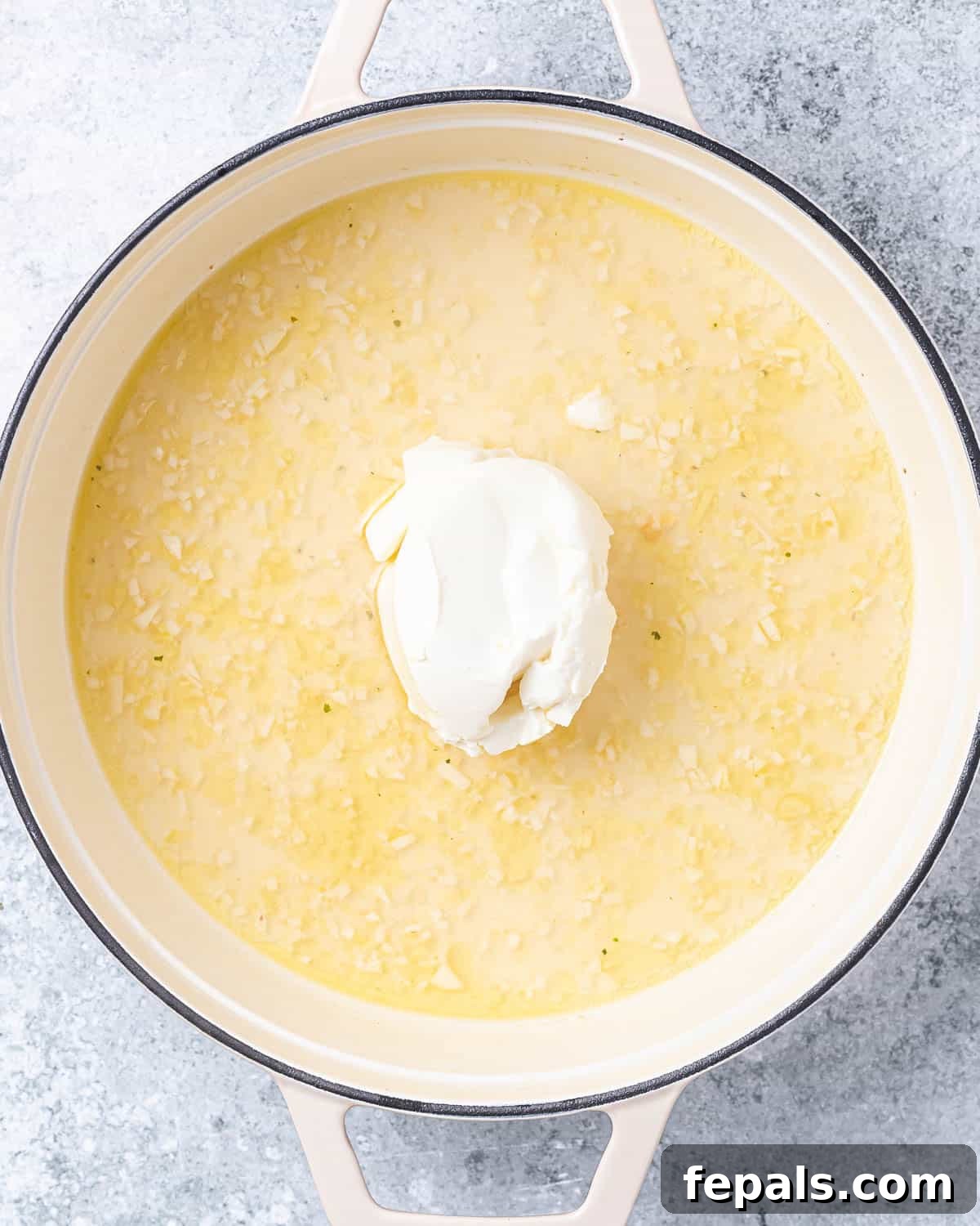 A pan with sautéed garlic, vegetable stock bubbling, and cream cheese melting, forming a rich, creamy sauce.
