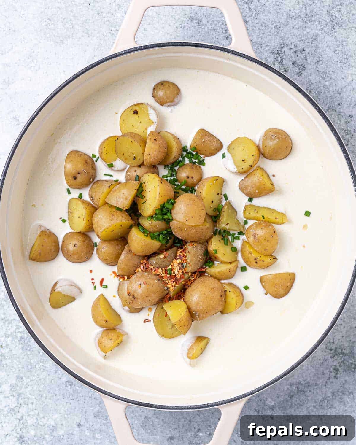 Tender baby potatoes and fresh chives stirred into a luxurious white cream sauce in a large skillet.