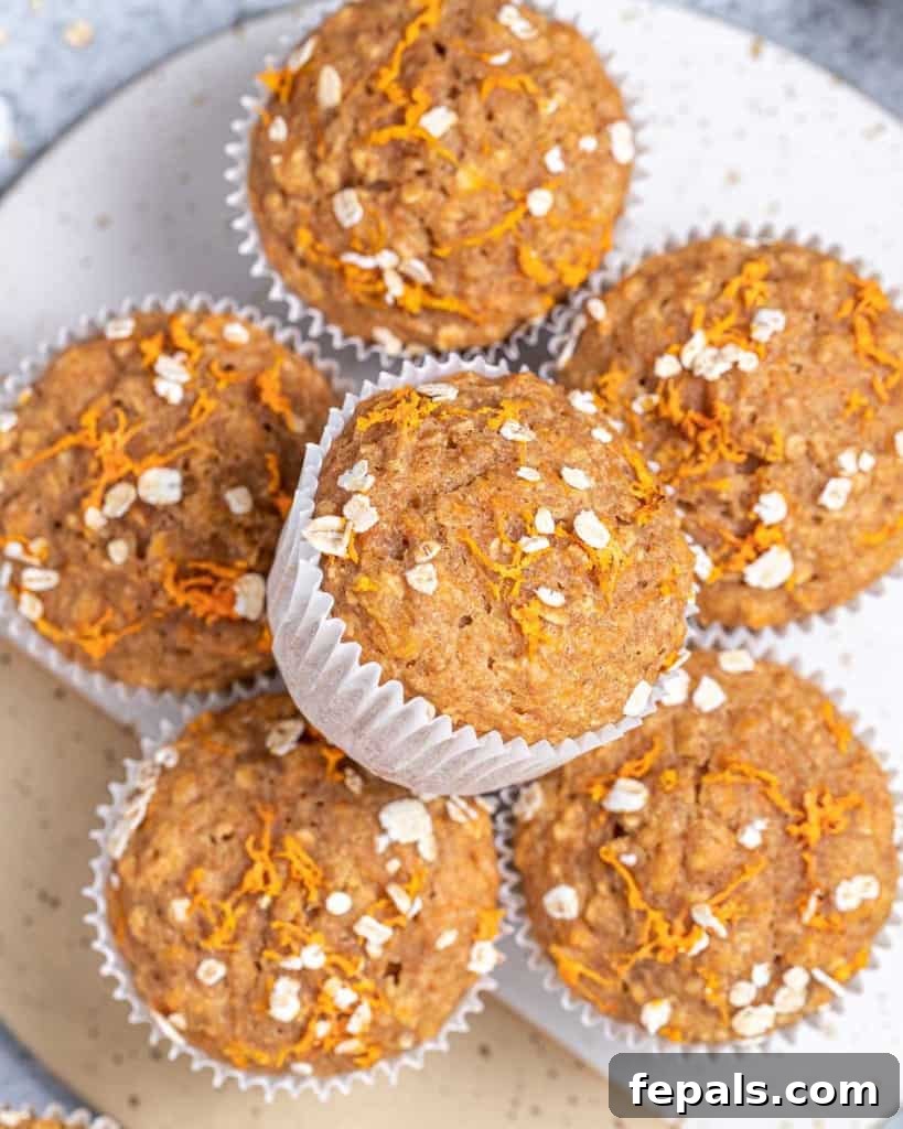 Close-up of fluffy carrot muffins in paper liners, visibly containing oats and shredded carrots.