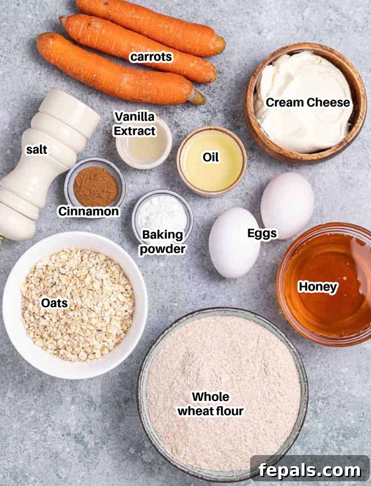 A flat lay showing all the fresh ingredients for carrot cake muffins, including flour, oats, carrots, eggs, honey, and cream cheese.