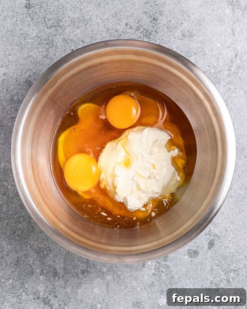 A bowl with wet ingredients such as eggs, honey, and cream cheese being whisked together until smooth.