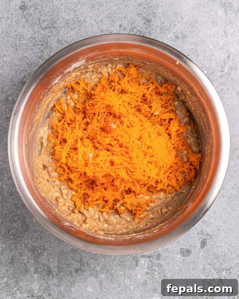 Folding shredded carrots into the muffin batter to ensure even distribution.