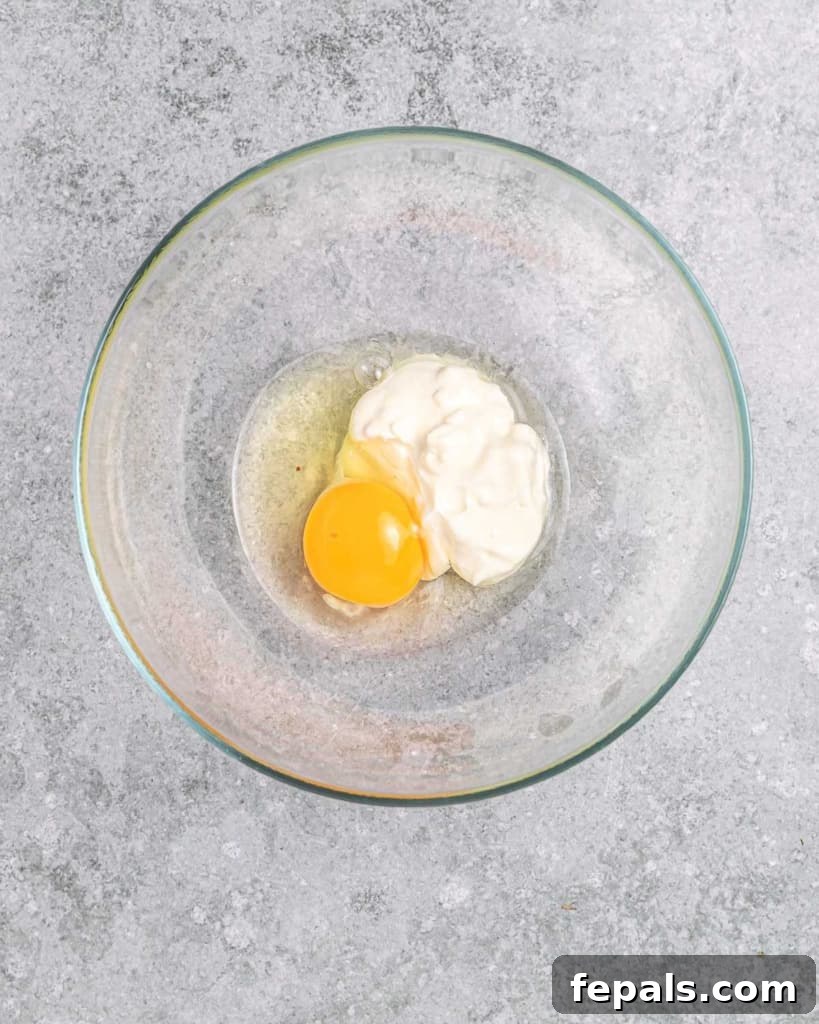 A visual of mixing a large egg with softened cream cheese in a medium bowl until smooth, demonstrating the preparation of wet ingredients.