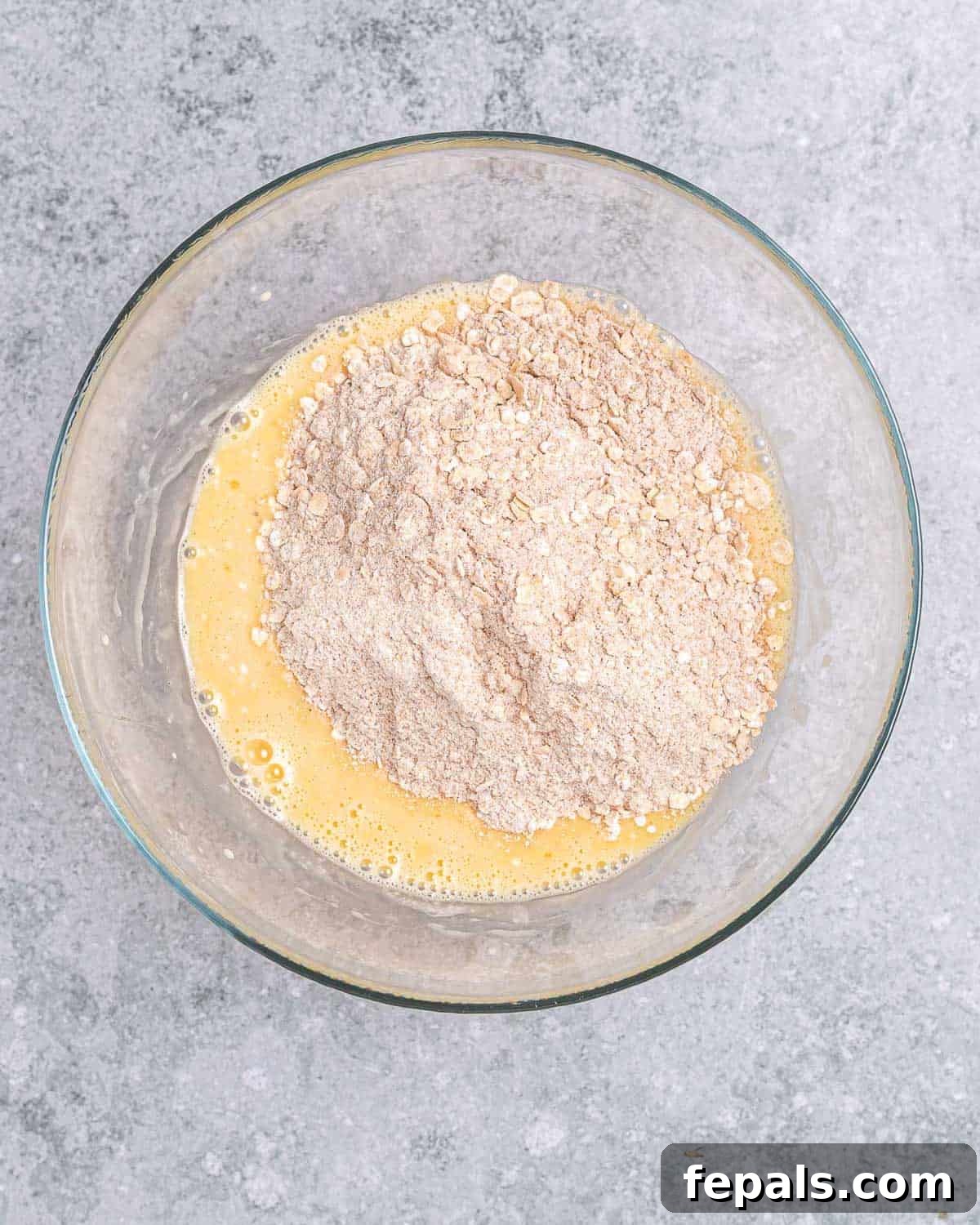A hand adding the dry flour mixture to the wet mixture in a large bowl, demonstrating the combination step of the cookie dough.