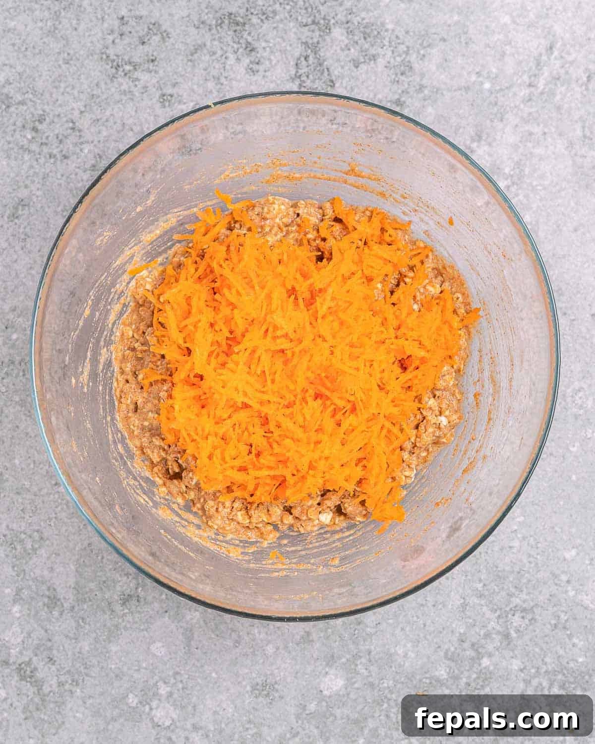 Shredded carrots being carefully folded into the cookie dough batter with a spatula, ensuring even distribution.