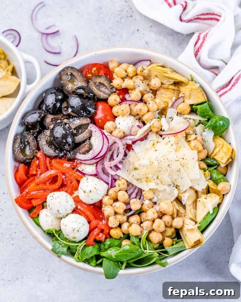 Classic Antipasto Salad 2 A vibrant Antipasto Salad featuring various colorful vegetables, chickpeas, juicy tomatoes, briny olives, crisp red onion, creamy parmesan, and fresh mozzarella cheese pearls, ready to be enjoyed.