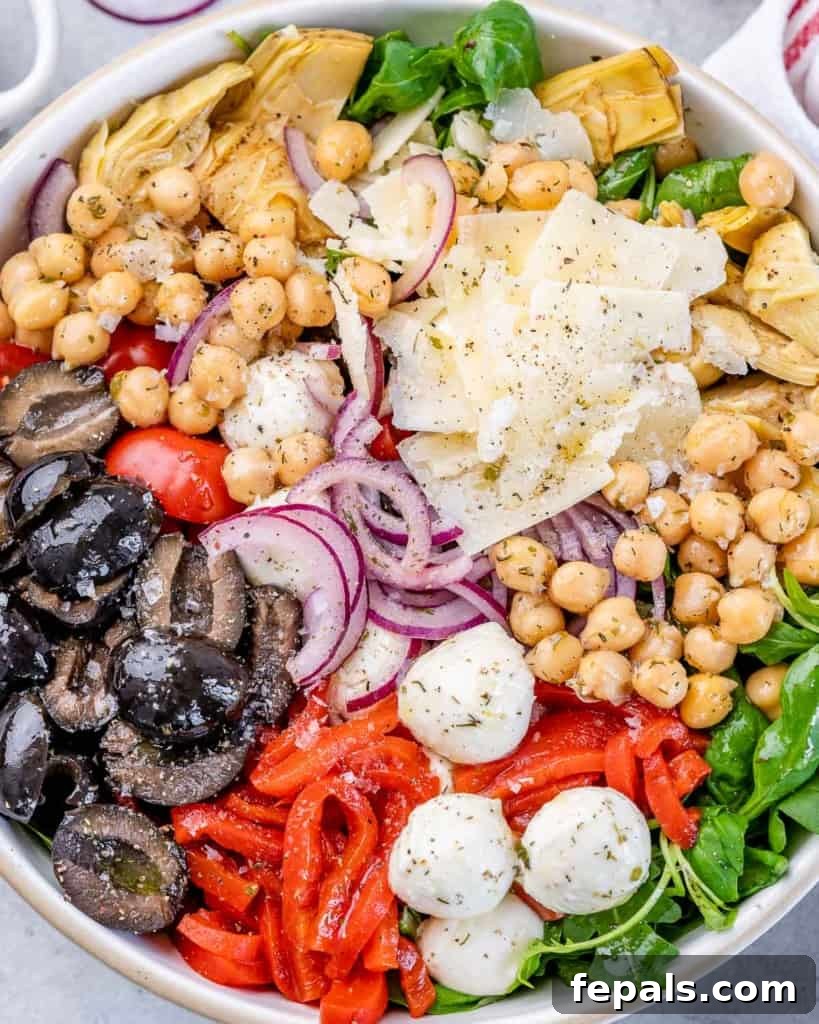 Classic Antipasto Salad 3 Freshly prepared Antipasto Salad in a rustic bowl, featuring chickpeas, various colorful olives, sweet roasted red peppers, and a bed of peppery arugula, showcasing its fresh ingredients.