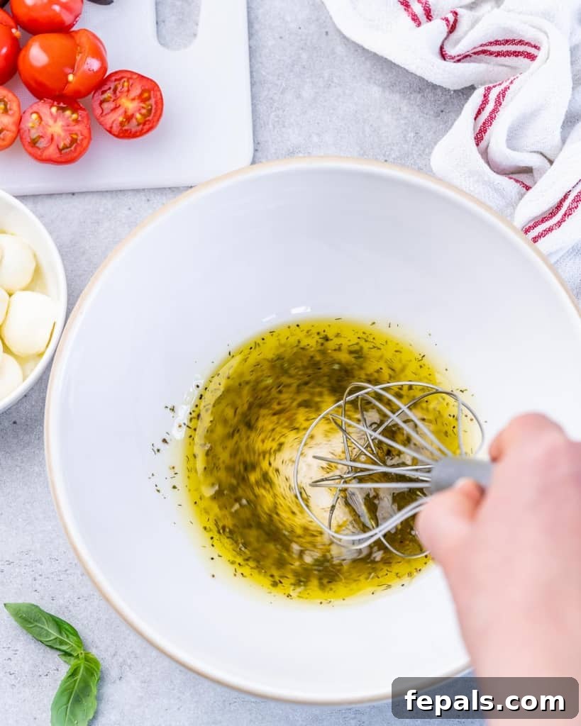 Classic Antipasto Salad 5 A close-up view of hands whisking together the dressing ingredients in a pristine white bowl, showcasing the emulsification process.