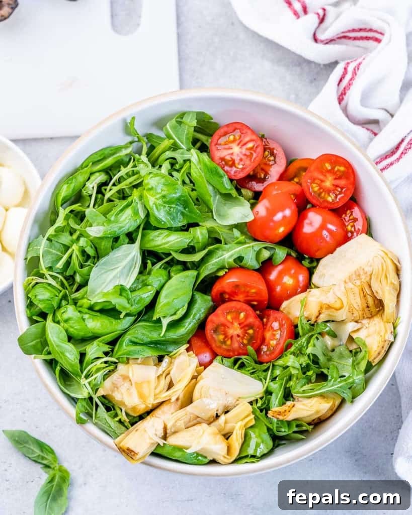 Classic Antipasto Salad 7 Hands carefully adding fresh arugula, juicy tomatoes, and tender artichoke hearts into a large bowl, building layers of fresh ingredients.