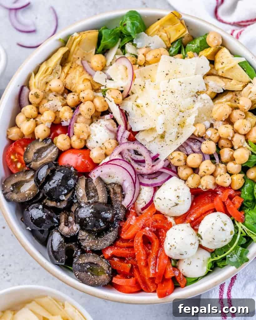 Classic Antipasto Salad 10 A vibrant close-up of Antipasto Salad, showcasing fresh arugula topped with dark black olives, sweet roasted red peppers, healthy chickpeas, and delicate shaved Parmesan cheese, highlighting its rich textures and colors.