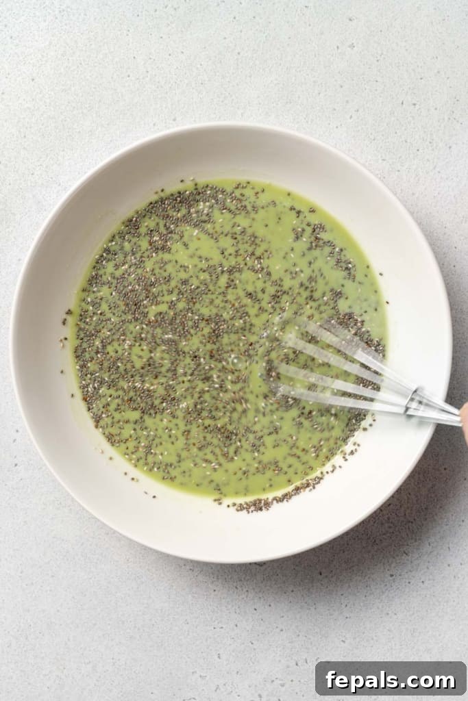 A whisk actively stirs the chia seeds into the matcha milk, ensuring thorough mixing and preventing clumping for an ideal pudding texture.