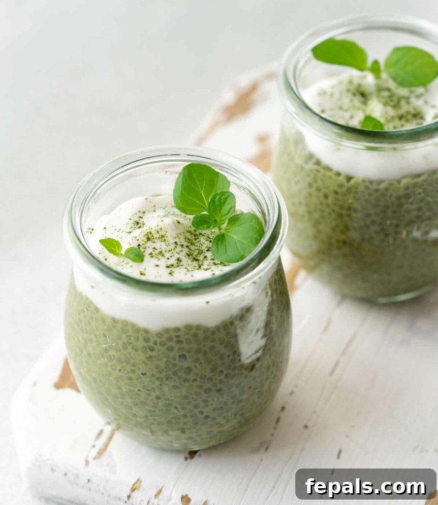 A vibrant side view of a jar of matcha chia pudding, elegantly topped with creamy yogurt and a dusting of matcha powder, showcasing its appetizing appeal.