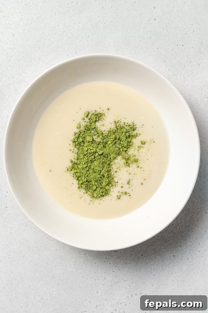 A close-up shot of matcha powder delicately resting on the surface of the milk mixture before being incorporated.