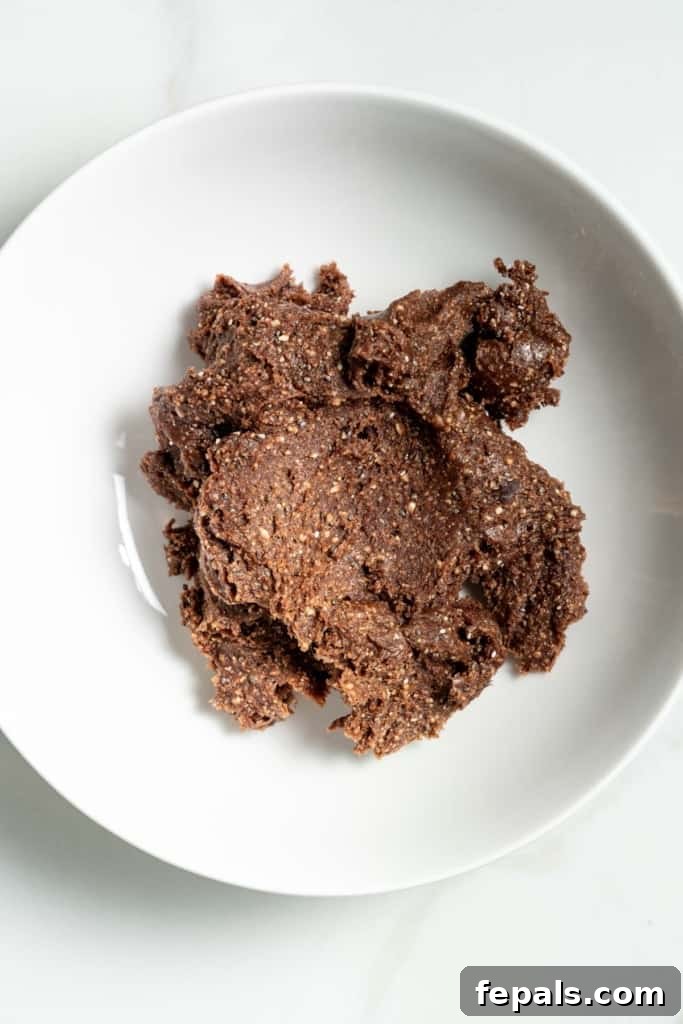 Decadent Double Chocolate Date Energy Bites 7 The chocolate ball mixture being transferred from a blender to a mixing bowl.