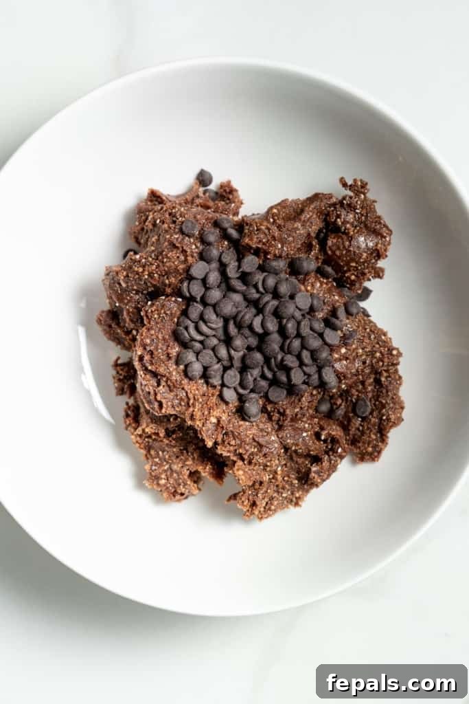 Decadent Double Chocolate Date Energy Bites 8 Mini chocolate chips being added and mixed into the chocolate ball mixture in a bowl.