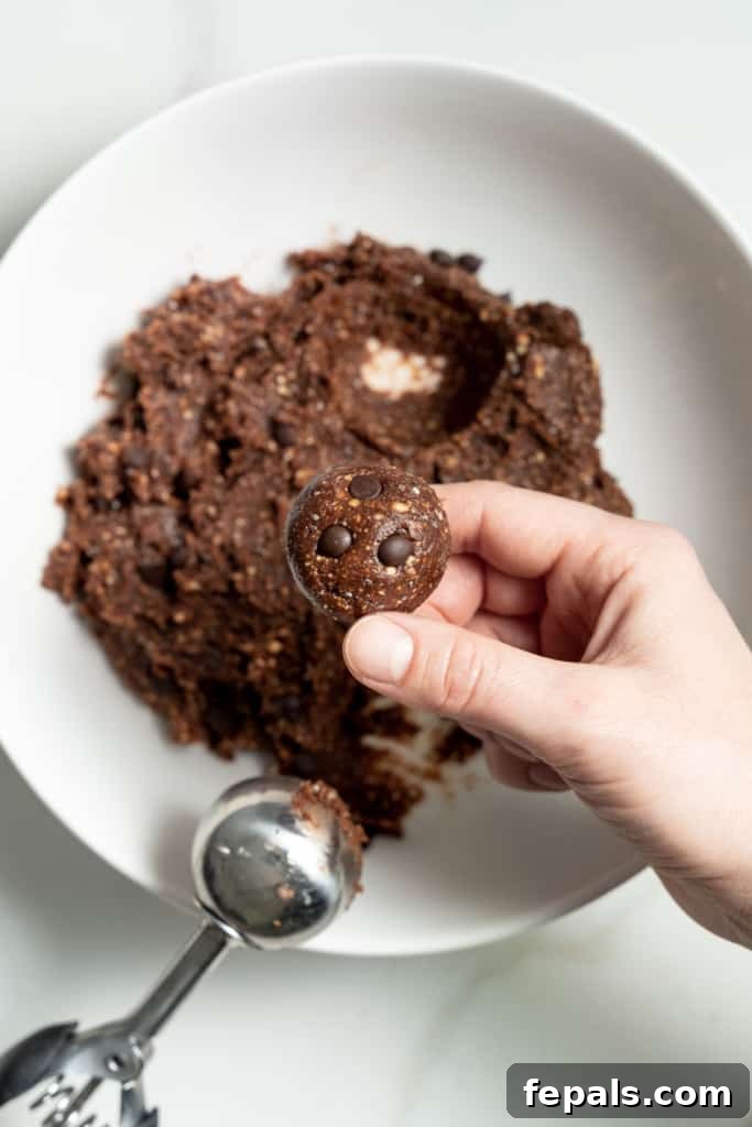 Decadent Double Chocolate Date Energy Bites 10 Hands rolling a portion of the double chocolate chip date energy ball mixture into a smooth, round shape.
