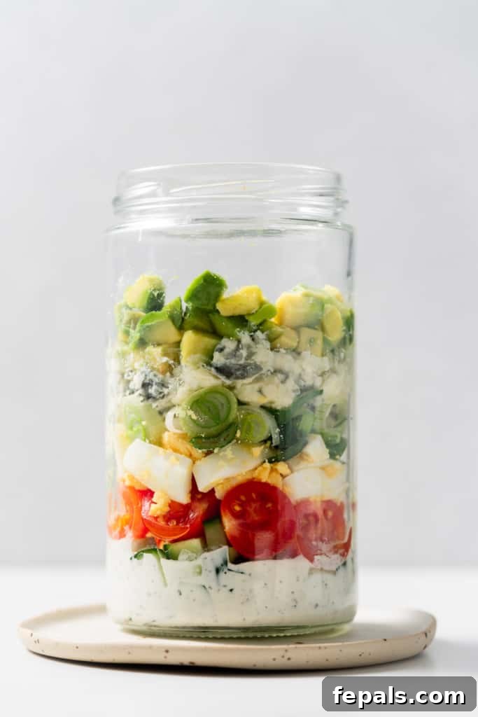 Plant-Powered Cobb Salad 10 Filling a glass jar with tomatoes, cheese and avocado.