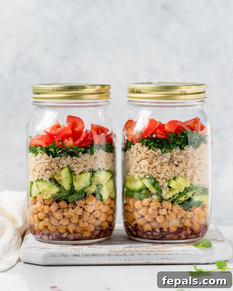 Refreshing Layered Chickpea Cucumber Jar 2 Two vibrant salad jars featuring layered chickpeas, cucumber, quinoa, fresh herbs, and cherry tomatoes, ready for a healthy meal.