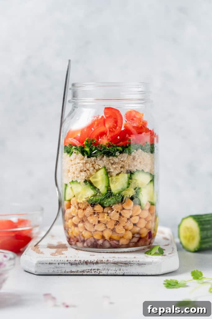 Refreshing Layered Chickpea Cucumber Jar 11 A beautifully assembled jar salad with its lid removed, placed next to a fork, inviting you to enjoy a fresh meal.